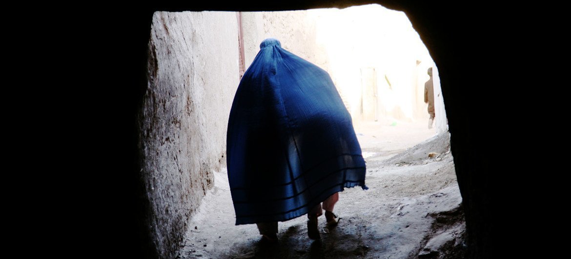 An Afghan woman walks through a narrow alley in Herat, carrying a child under her burqa.